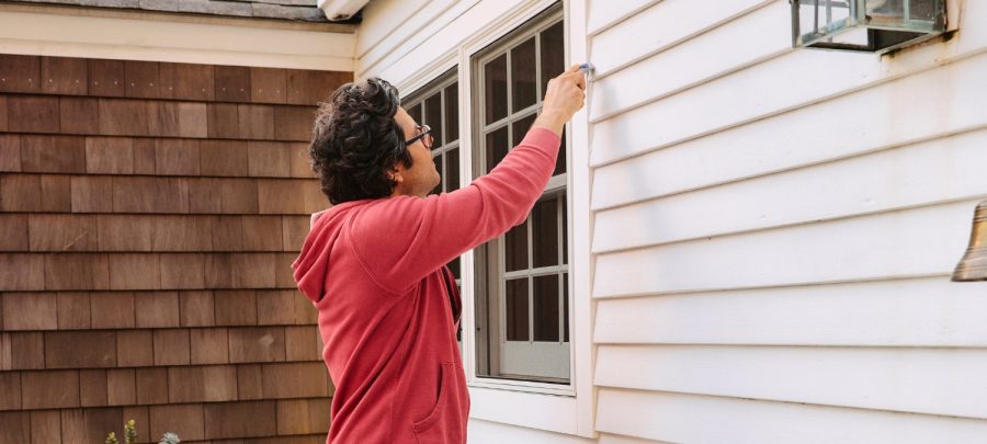A landlord inspecting old, failing sealant on an exterior window frame.
