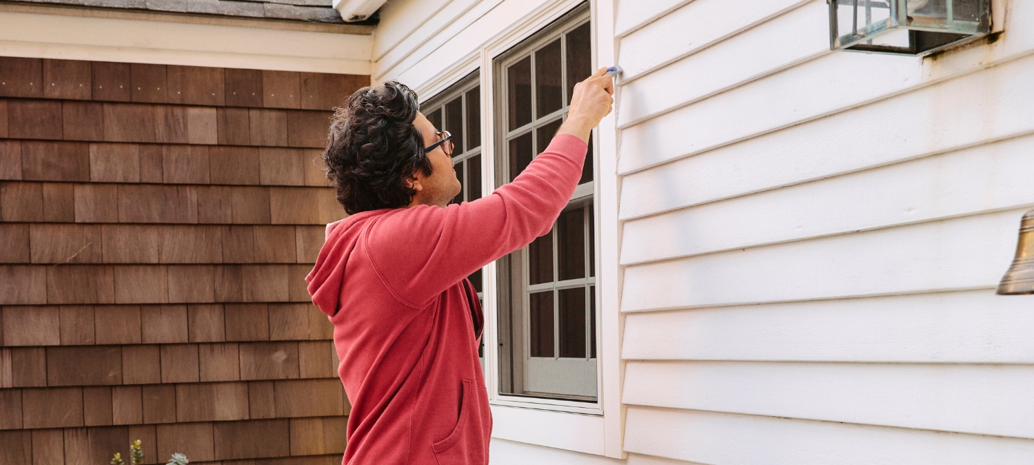 A landlord inspecting old, failing sealant on an exterior window frame.