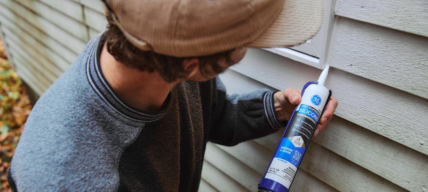 Man completing home maintenance tasks by sealing around exterior window using GE Supreme Silicone Window & Door Sealant.