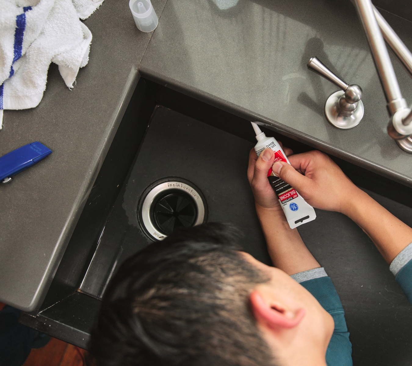 DIYer laying silicone sealant at a bathroom sink after testing for cracks or edge lift.