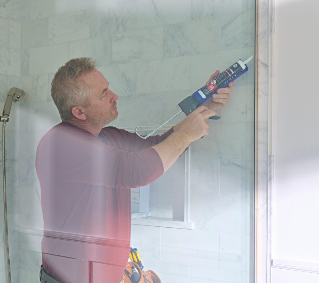 Homeowner applying a bead of GE Pro Seal Max Kitchen & Bath Sealant along a shower edge.