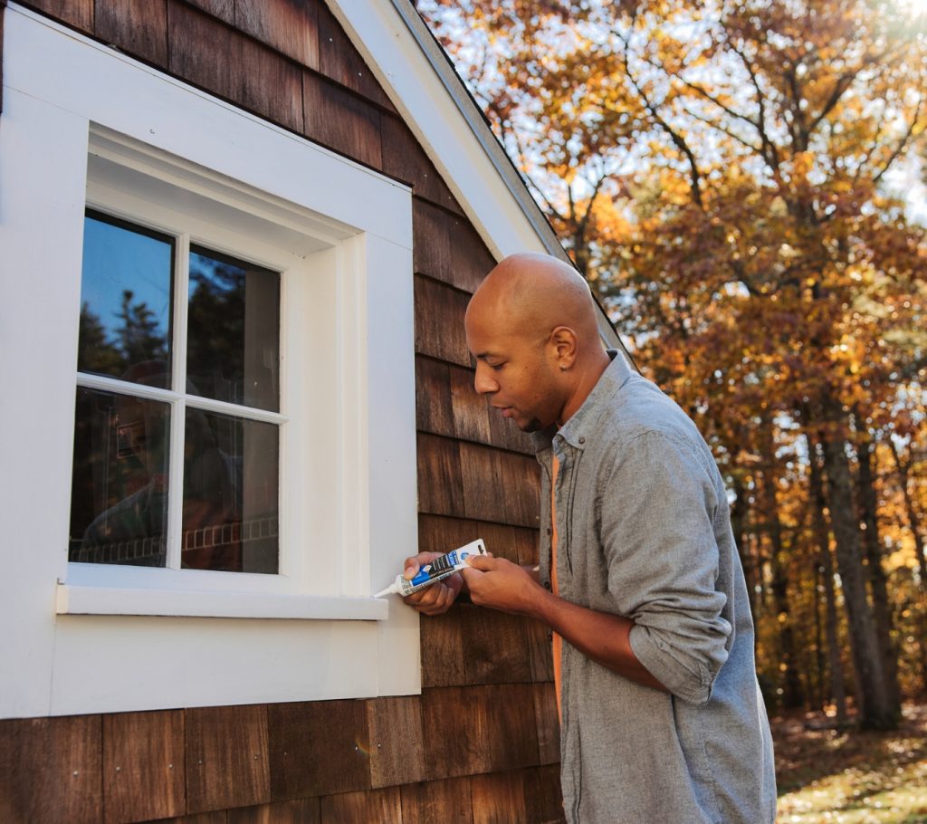 Man is applying GE Supreme Silicone Window & Door Sealant around exterior window.
