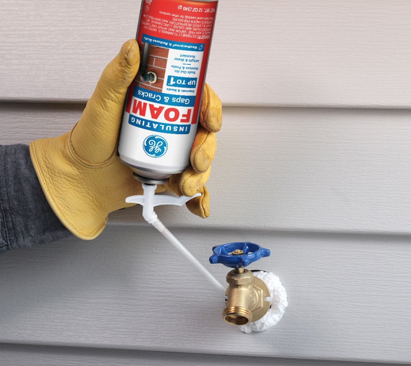 Homeowner sealing gaps around an exterior hose bib with GE Gaps & Cracks insulating foam. 