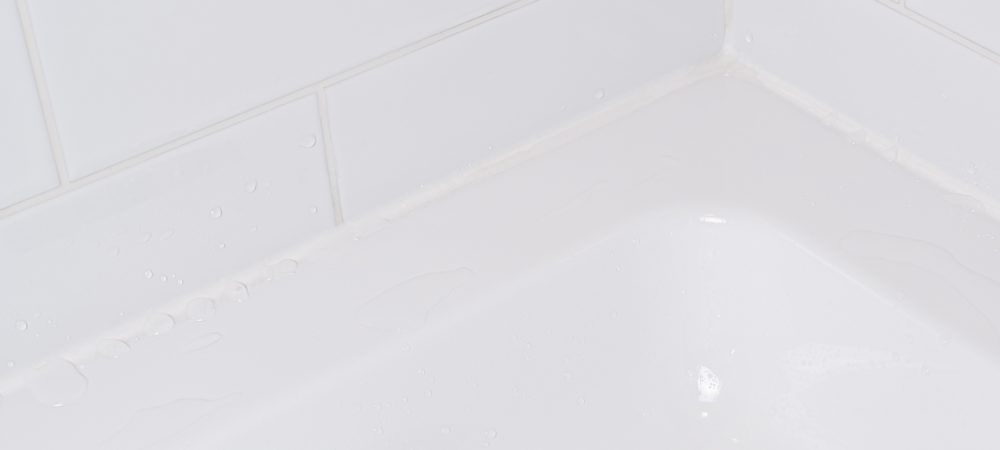 Close-up shot of a clean, slightly concave GE Supreme Silicone Kitchen & Bath Sealant bead at a tub-to-tile seam.