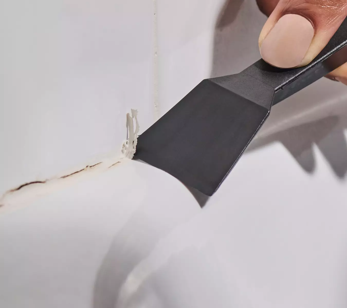 A photo of a homeowner removing old sealant with GE’s Sealant Remover Tool.