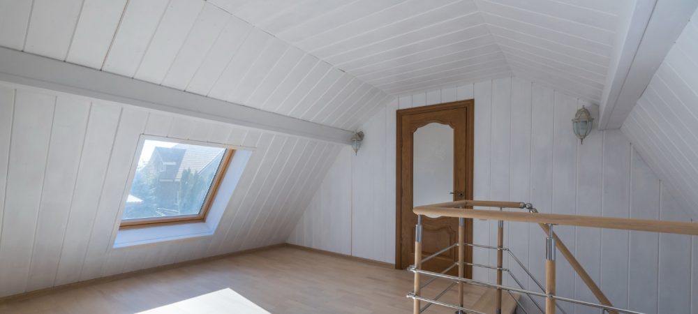 A bright attic-style room features white panel walls, a skylight window, and warm natural light.