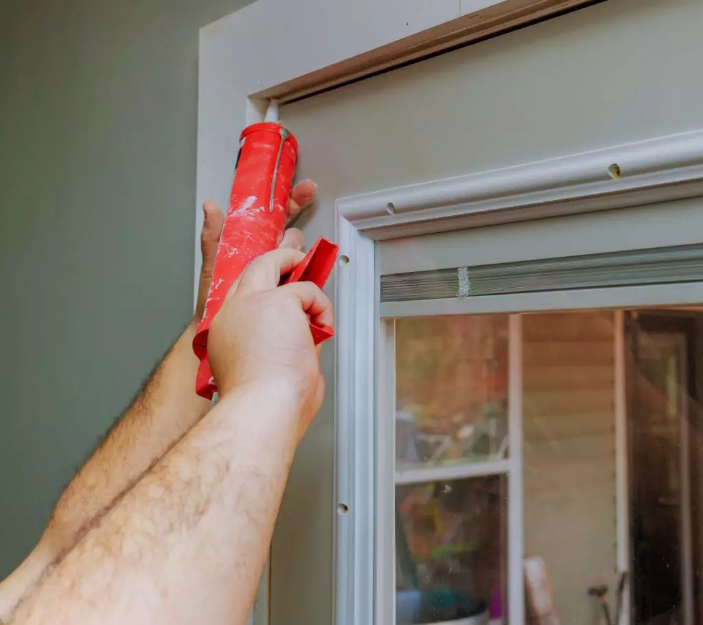 A photo of a homeowner applying sealant along the perimeter joint of an interior window frame.