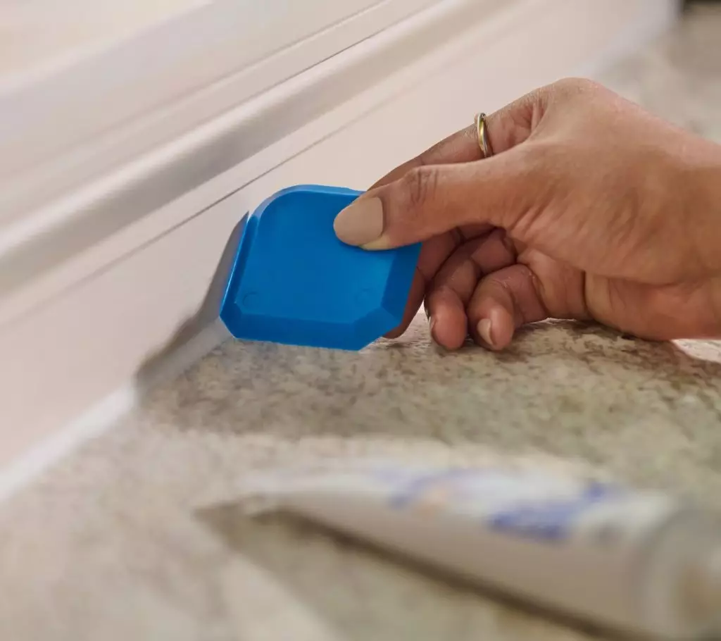 A close-up of a person using the Sealant Smoothing Tool on a fresh bead along trim edge