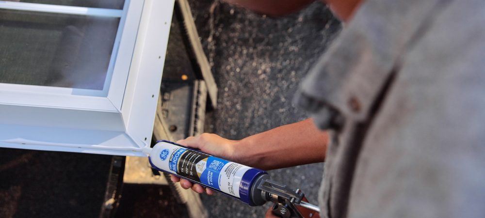 A photo of a homeowner applying sealant to a window frame.