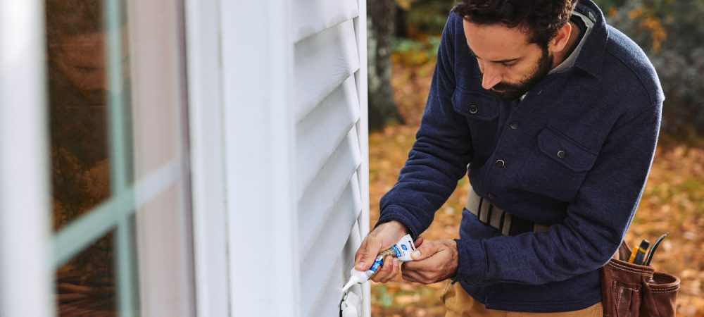 Man considering sealant cure time and applying silicone sealant on the exterior of the home.