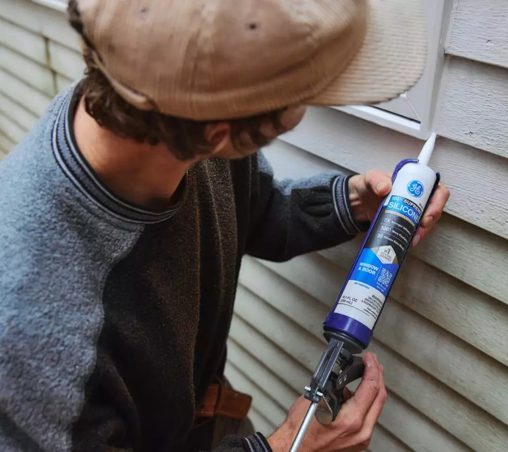 Man applying silicone sealant around an exterior window of the home.