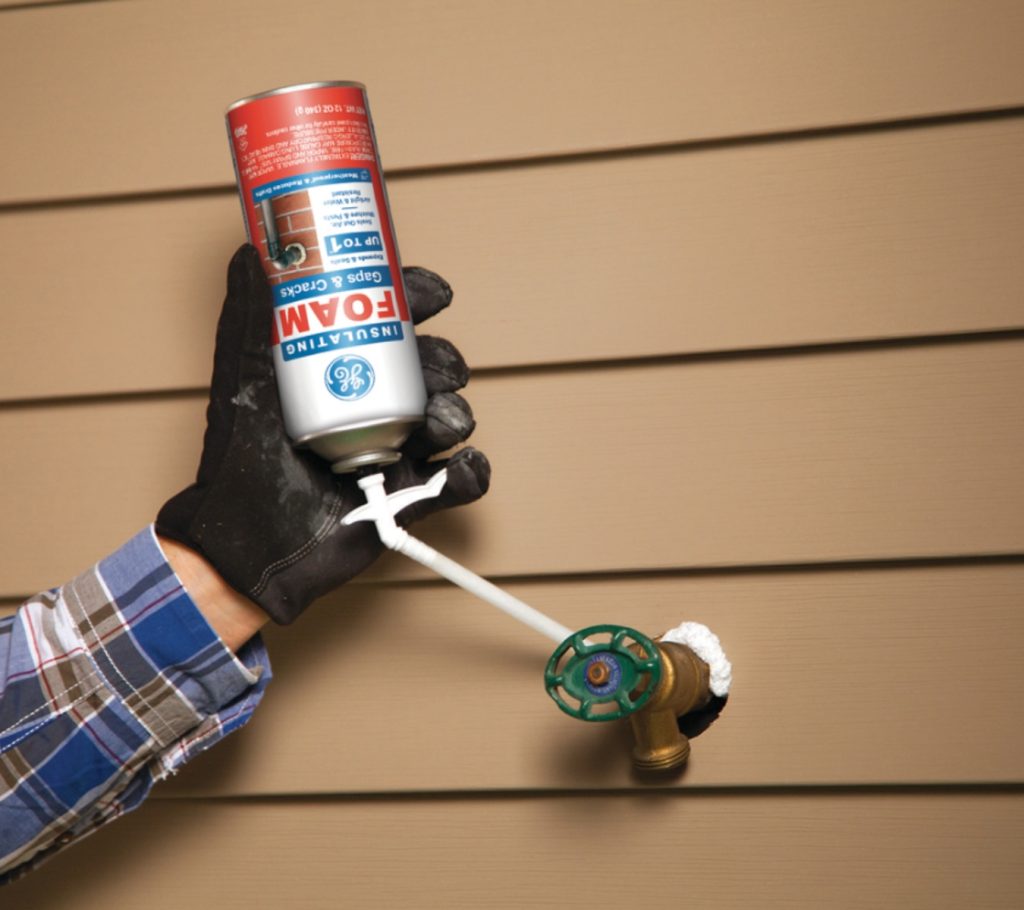 A contractor applying GE Gaps & Cracks Insulating Foam around an exterior faucet penetration in house siding.