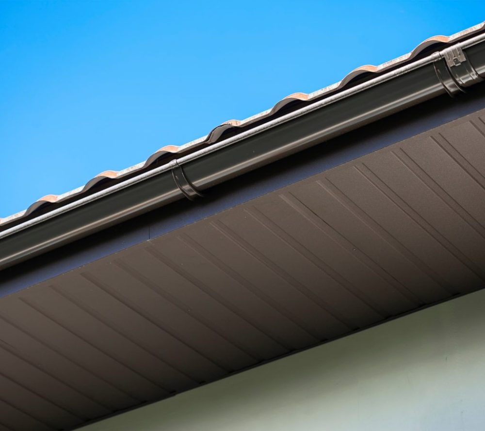 Dark roof gutter with visible section joints beneath a tiled roof